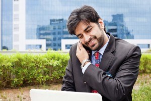 A man sitting in the park on his phone and on his laptop