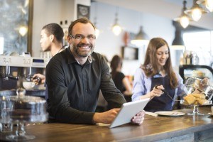 a cafe owner stands behind the counter of his coffee shop and smiles