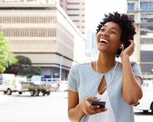 Portrait of smiling young african american woman listening to music on headphones outdoors on city street