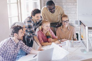 A group of co-workers huddled around a large computer screen