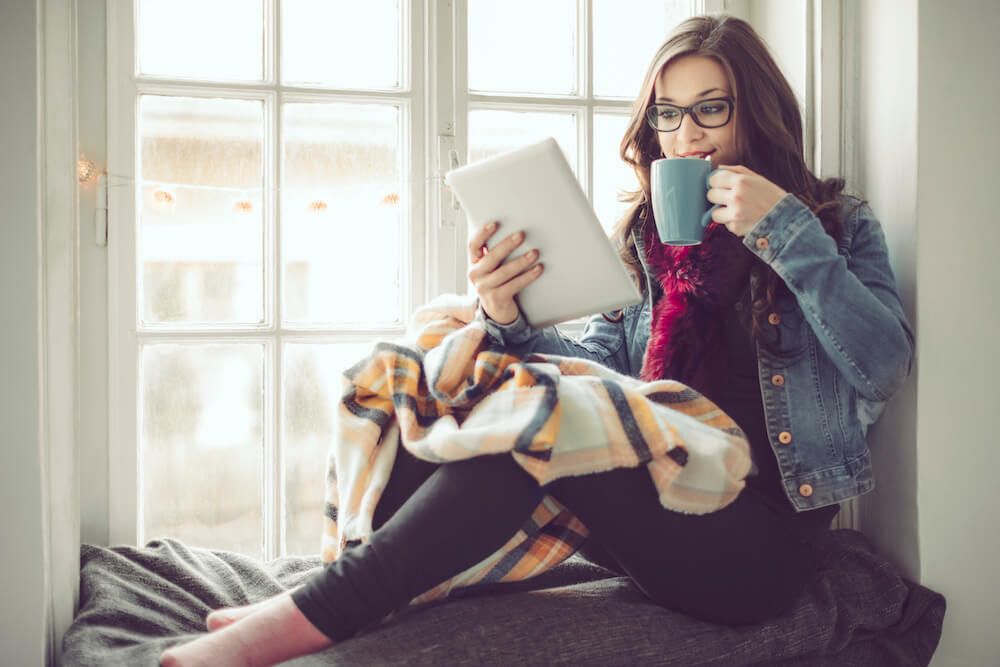 Young woman working from home with coffee, blanket and tablet